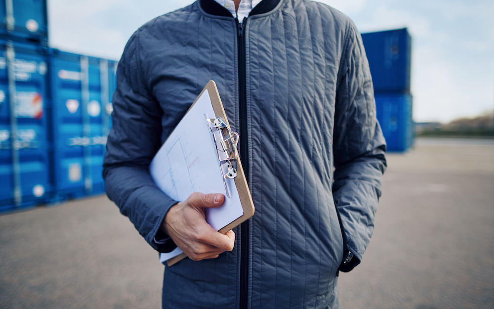 foreman-standing-in-a-shipping-yard-holding-an-inv-2024-09-22-16-30-12-utc